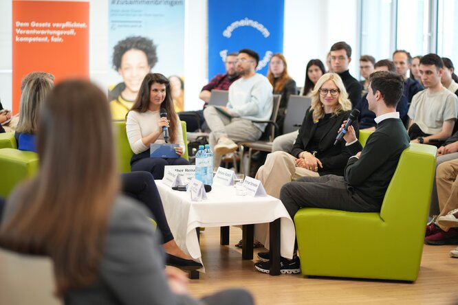 Diskussion mehrerer Personen auf grünen Stühlen in der Mitte des Publikums.